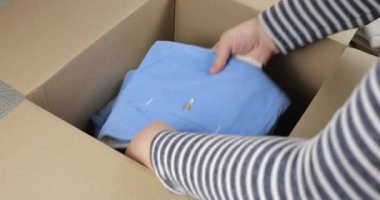 Bir kadın, erkek ve kadın kıyafetlerini karton bir kutuya koyar. Giysileri depolama, taşıma, sıralama, postalama veya bağışlama konularında. Günlük kotlar, pantolonlar, şortlar, gömlekler, tişörtler, bluzlar, uzun kollular..