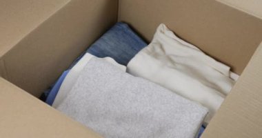 Bir kadın, erkek ve kadın kıyafetlerini karton bir kutuya koyar. Giysileri depolama, taşıma, sıralama, postalama veya bağışlama konularında. Günlük kotlar, pantolonlar, şortlar, gömlekler, tişörtler, bluzlar, uzun kollular..