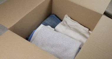 Bir kadın, erkek ve kadın kıyafetlerini karton bir kutuya koyar. Giysileri depolama, taşıma, sıralama, postalama veya bağışlama konularında. Günlük kotlar, pantolonlar, şortlar, gömlekler, tişörtler, bluzlar, uzun kollular..