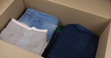 Bir kadın kot pantolon, sıcak süveter, eşarp ve şapkaları karton bir kutuya koyar. Giysileri depolama, taşıma, sıralama, postalama veya bağış konularında içerik.