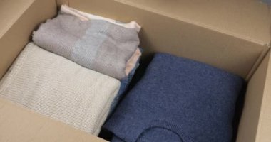Bir kadın kot pantolon, sıcak süveter, eşarp ve şapkaları karton bir kutuya koyar. Giysileri depolama, taşıma, sıralama, postalama veya bağış konularında içerik.