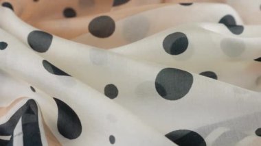 Yumuşak kıvrımlı, açık bej renginde, doğal ipekten yapılmış, siyah benekli, vitrinde döndürülmüş en ince kumaş. Moda, tasarım, aksesuarlar konularında tekstil arka planı.