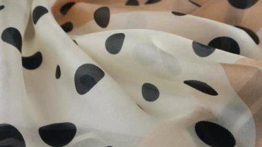 Yumuşak kıvrımlı, açık bej renginde, doğal ipekten yapılmış, siyah benekli, vitrinde döndürülmüş en ince kumaş. Moda, tasarım, aksesuarlar konularında tekstil arka planı.