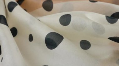 Yumuşak kıvrımlı, açık bej renginde, doğal ipekten yapılmış, siyah benekli, vitrinde döndürülmüş en ince kumaş. Moda, tasarım, aksesuarlar konularında tekstil arka planı.
