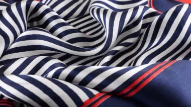 Vitrinde dönen koyu mavi, beyaz ve kırmızı çizgili yumuşak katlanmış ipek kumaşın yakın plan görüntüsü. Moda, tasarım, aksesuarlar konularında tekstil arka planı.