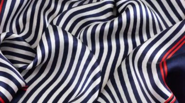 Yumuşak kıvrımlı ipek kumaşın üst görüntüsü vitrinde koyu mavi, beyaz ve kırmızı çizgilerle döndürüldü. Moda, tasarım, aksesuarlar konularında tekstil arka planı.