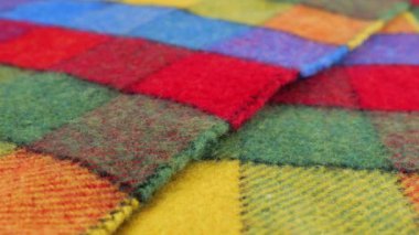 Ekran kılıfında dönen büyük bir çekteki parlak desenli çok renkli yün kumaşın yakın görüntüsü. Soğuk hava, sıcak kıyafetler, konfor, aksesuarlar ve tasarım teması üzerine tekstil arka planı.