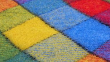 Ekran kılıfında dönen büyük bir çekteki parlak desenli çok renkli yün kumaşın yakın görüntüsü. Soğuk hava, sıcak kıyafetler, konfor, aksesuarlar ve tasarım teması üzerine tekstil arka planı.