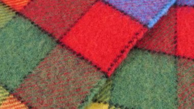 Parlak desenli çok renkli yün kumaşın üst görüntüsü vitrinde döndürülmüş büyük bir çekle. Soğuk hava, sıcak kıyafetler, konfor, aksesuarlar ve tasarım teması üzerine tekstil arka planı.