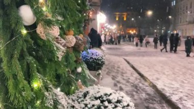 Noel dekorunun arka planında, kozalaklı dallar, elektrik çelenkleri ve şehirdeki diğer dekorlar şeklinde kar yağıyor.