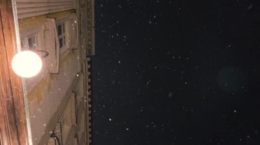 Kar, karanlık bir gökyüzünün arka planına, bir binaya ve parlayan bir sokak lambasına düşer..