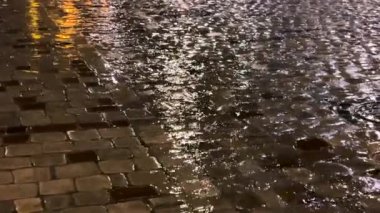 Su birikintileri, su dereleri, gece yağmur sırasında lambalardan yansıyan ışık. Şehrin kaldırımlı caddesi..