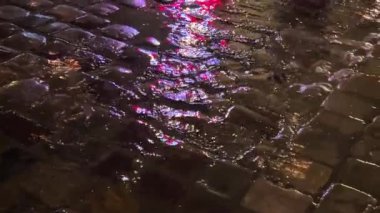 Su birikintileri, su dereleri, gece yağmur sırasında lambalardan yansıyan ışık. Şehrin kaldırımlı caddesi..