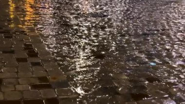 Su birikintileri, su dereleri, gece yağmur sırasında lambalardan yansıyan ışık. Şehrin kaldırımlı caddesi..
