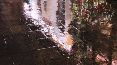 Su birikintileri, su dereleri, gece yağmur sırasında lambalardan yansıyan ışık. Şehrin kaldırımlı caddesi..