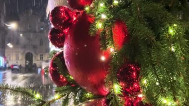 Çelenk ve aydınlatmayla süslenmiş bir Noel ağacının arka planına doğru yağmur yağıyor. Akşamları çekim..