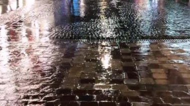 Su birikintileri, su dereleri, gece yağmur sırasında lambalardan yansıyan ışık. Şehrin kaldırımlı caddesi..