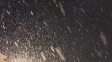 Kar, karanlık bir gökyüzünün arka planına, bir binaya ve parlayan bir sokak lambasına düşer..