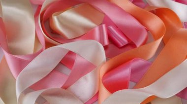 Saten renkli kurdeleler vitrinde döner. Aksesuar teması, el işi, tasarım, moda, el yapımı. Pembe ve şeftali rengi kurdeleler..