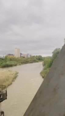 Nehrin tren penceresinden ve nehrin karşısındaki köprünün metal desteklerinden görüntüyü al. Dikey video.