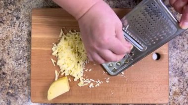 Büyük metal bir rende rendelenmiş peyniri tahta bir tahtaya karşı rendelemek. Üst görünüm.