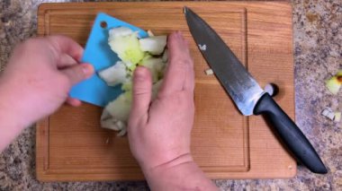 Doğranmış soğan daha fazla pişirmek için mutfak spatulasıyla ahşap kesme tahtasından çıkarılır. Üst görünüm.