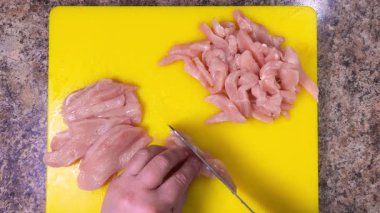 Kesme tahtasında satırla çiğ tavuk göğsünü dilimlemek. Üst görünüm.