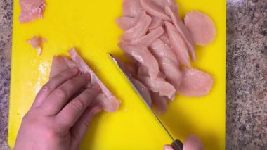 Kesme tahtasında satırla çiğ tavuk göğsünü dilimlemek. Üst görünüm.