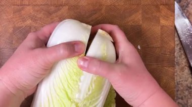 Napa lahanası bir bıçakla yarı yarıya kesilir ve salata için ahşap bir kesme tahtasında ince ince doğranır. Üst görünüm.