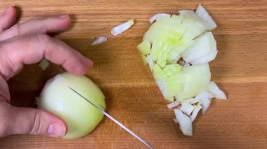 Tahta bir kesme tahtasının üzerinde bıçakla soğanları küçük küplere ayırmak. Üst görünüm.