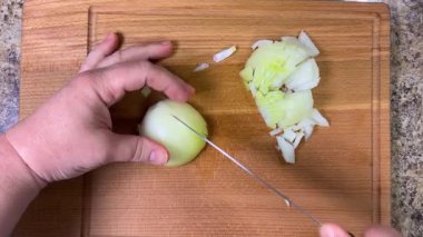 Tahta bir kesme tahtasının üzerinde bıçakla soğanları küçük küplere ayırmak. Üst görünüm.