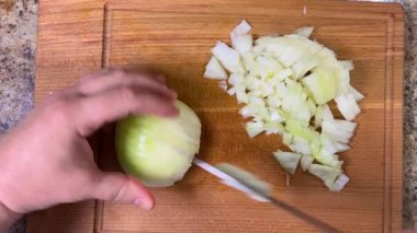 Tahta bir kesme tahtasının üzerinde bıçakla soğanları küçük küplere ayırmak. Üst görünüm.