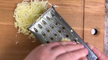 Büyük metal bir rende rendelenmiş peyniri tahta bir tahtaya karşı rendelemek. Üst görünüm.