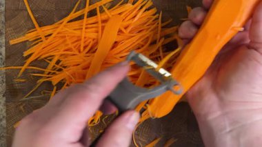 Ahşap kesme tahtasına havuç soyan bir kadın..