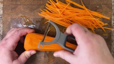 Ahşap kesme tahtasına havuç soyan bir kadın..