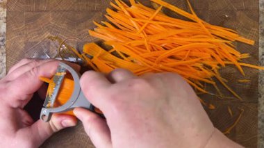 Ahşap kesme tahtasına havuç soyan bir kadın..