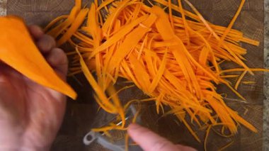 Ahşap kesme tahtasına havuç soyan bir kadın..