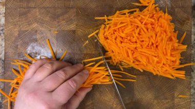 Şef, tahta kesme tahtasının üzerinde bıçakla doğranmış havuç doğruyor..