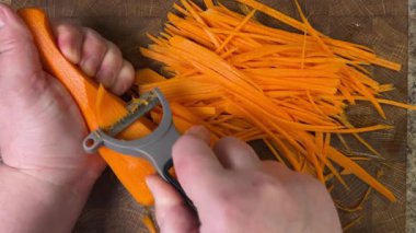 Ahşap kesme tahtasına havuç soyan bir kadın..