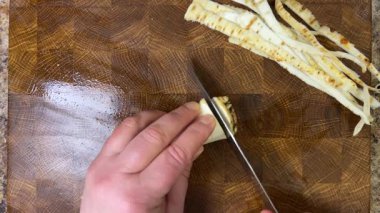 Bir aşçı, ağaç kesme tahtasına saplanmış bir bıçakla maydanoz kökü doğruyor..