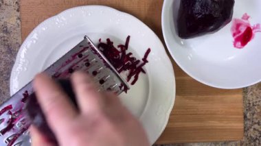 Beyaz tabak arka planında rendelenmiş pancar rendeleniyor.