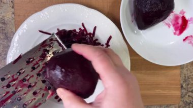 Beyaz tabak arka planında rendelenmiş pancar rendeleniyor.