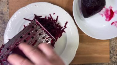 Beyaz tabak arka planında rendelenmiş pancar rendeleniyor.