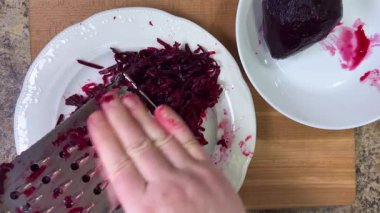 Beyaz tabak arka planında rendelenmiş pancar rendeleniyor.