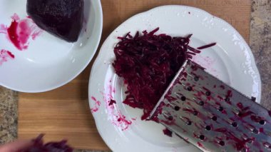 Beyaz tabak arka planında rendelenmiş pancar rendeleniyor.