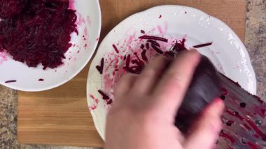 Beyaz tabak arka planında rendelenmiş pancar rendeleniyor.