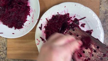 Beyaz tabak arka planında rendelenmiş pancar rendeleniyor.