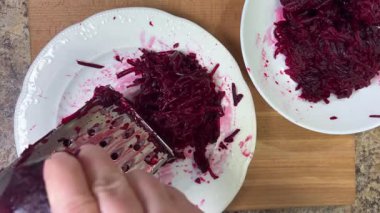 Beyaz tabak arka planında rendelenmiş pancar rendeleniyor.