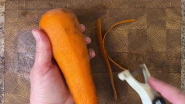 Ahşap kesme tahtasına havuç soyan bir kadın..