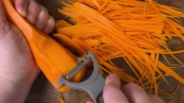 Ahşap kesme tahtasına havuç soyan bir kadın..